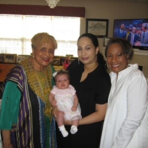 Three women posing with a baby in a living room.