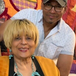 A man and woman posing for a photo in front of a colorful quilt.