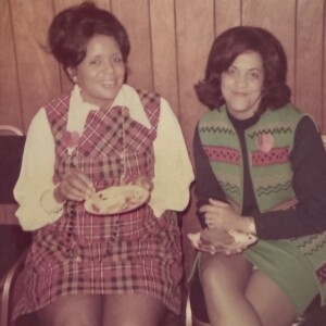 Two women sitting next to each other with plates of food.