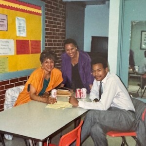 Three people sitting at a table in a classroom.