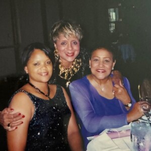 Three women posing for a picture at a dinner table.