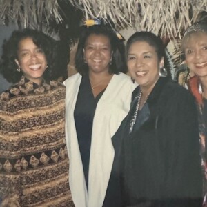 Four women posing for a photo in front of a thatched hut.