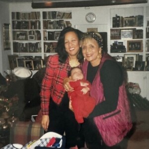 Two women holding a baby in a living room.