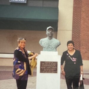 Two women standing next to a bust of a baseball player.