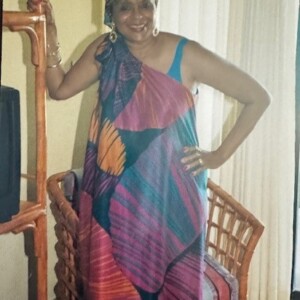 A woman in a colorful dress standing in front of a tv.