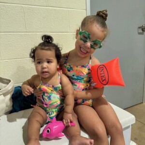 Two little girls in swimsuits sitting on a bench.